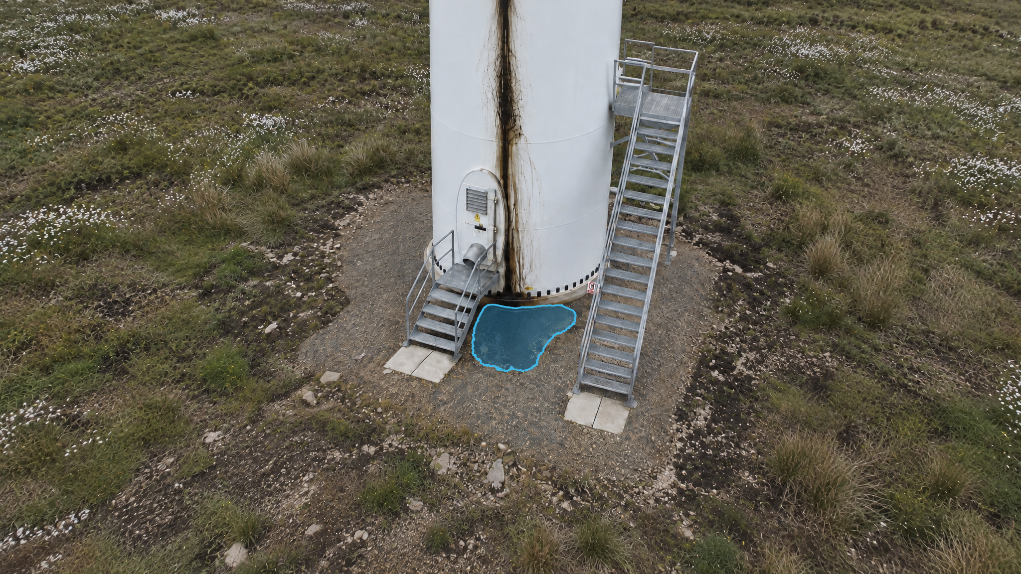 Wind turbine base with a dark streak down the tower and a blue detection overlay marking a puddle below the access door.