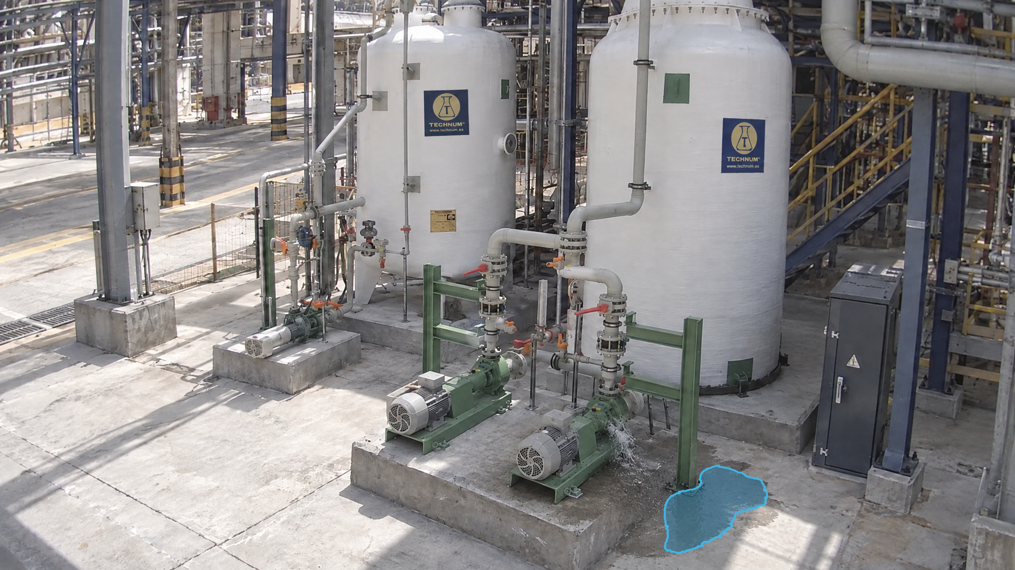 Pumps on a concrete pad beside process vessels, with a visible leak at a pump and a blue detection overlay marking the puddle beside the pad.