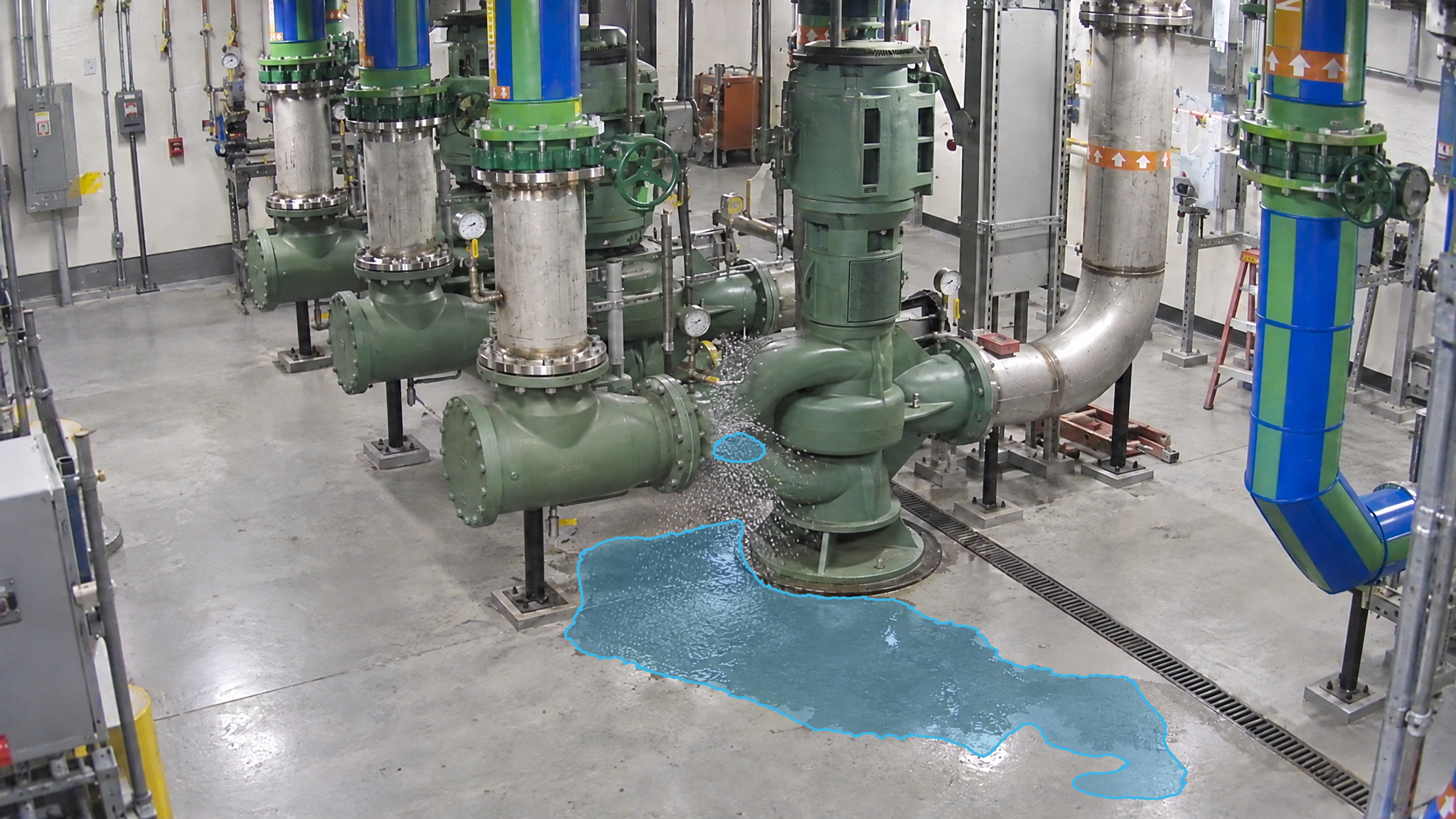 Pump room with spray beside a pump flange and blue detection overlays marking puddles on the floor.