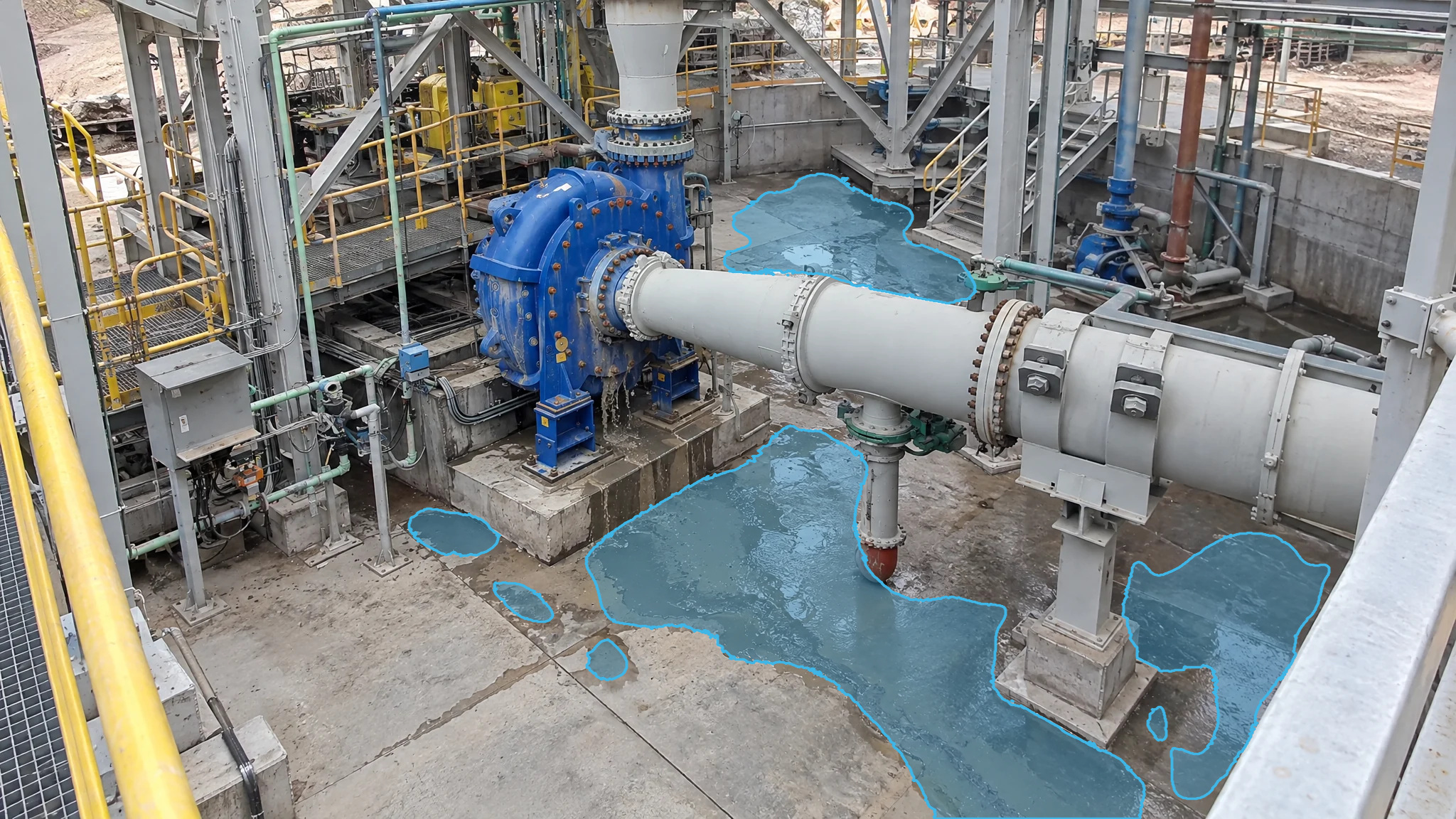 Blue slurry pump in a mill with blue detection overlays marking liquid pooling across the concrete floor.