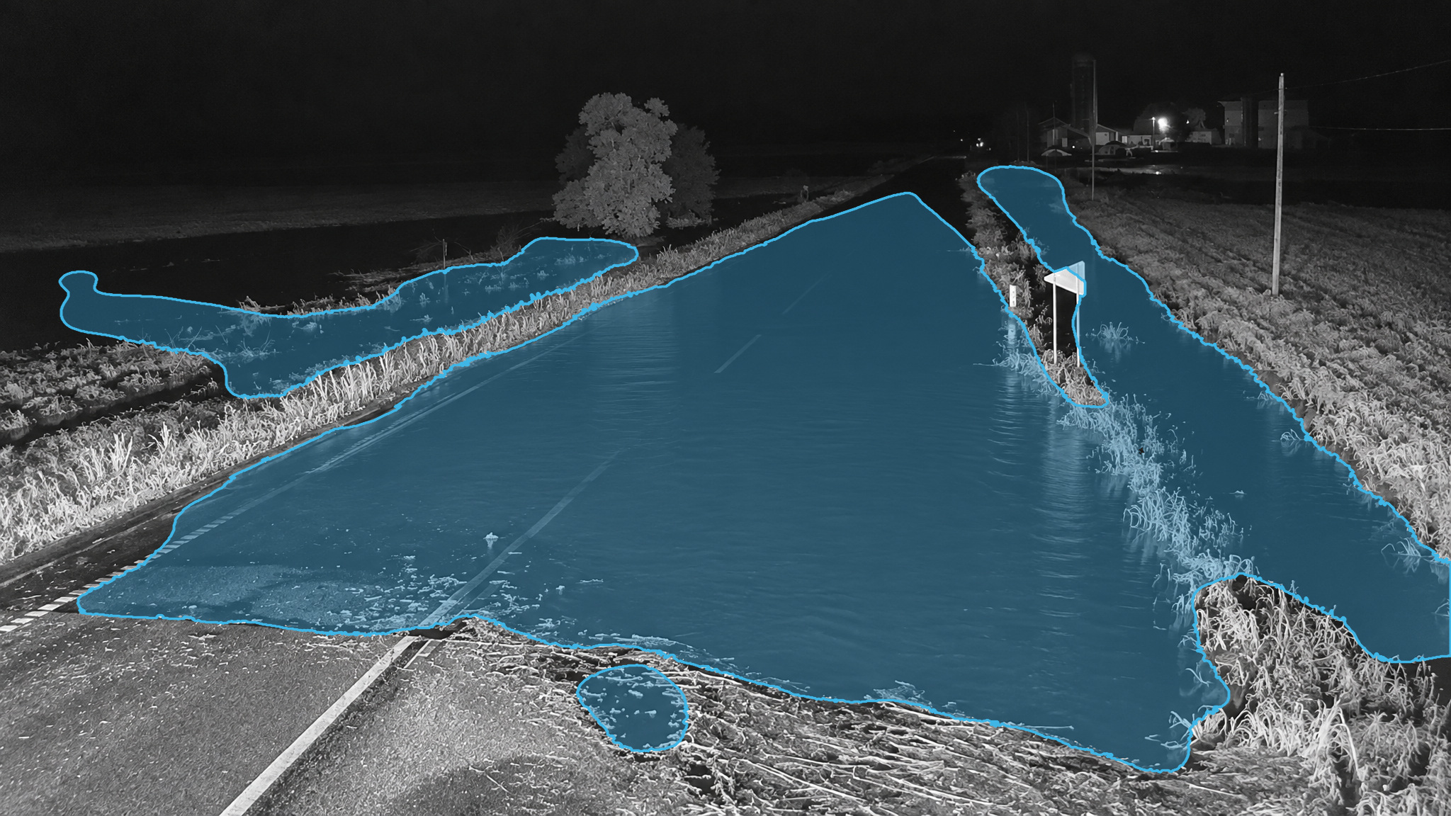 Flooded road in a near-infrared night frame. Blue detection overlay marks the standing water.