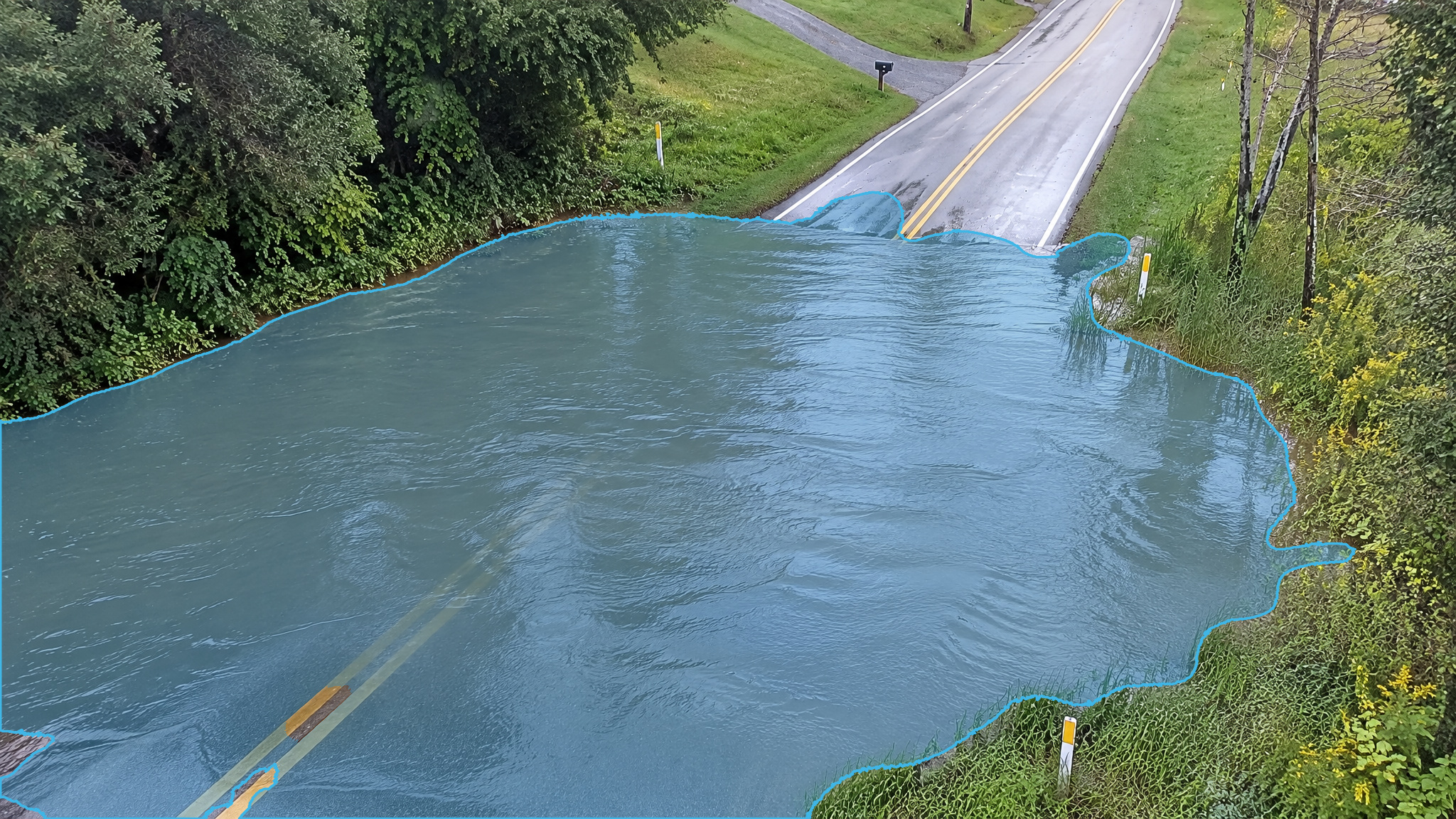 Flooded rural road in daylight. Blue detection overlay marks the standing water.