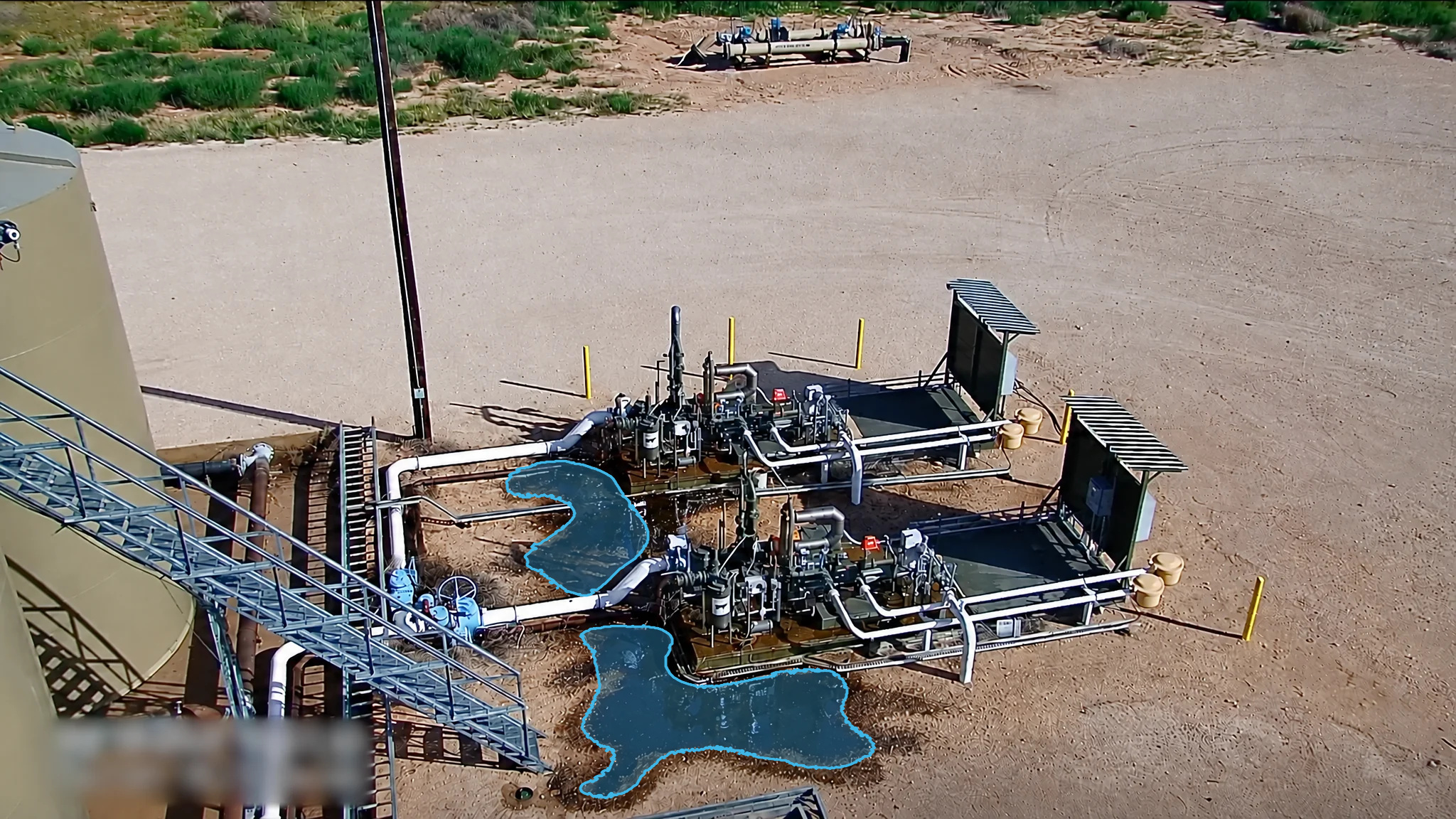 Elevated view of LACT units beside a storage tank with blue detection overlays marking puddles around the piping.
