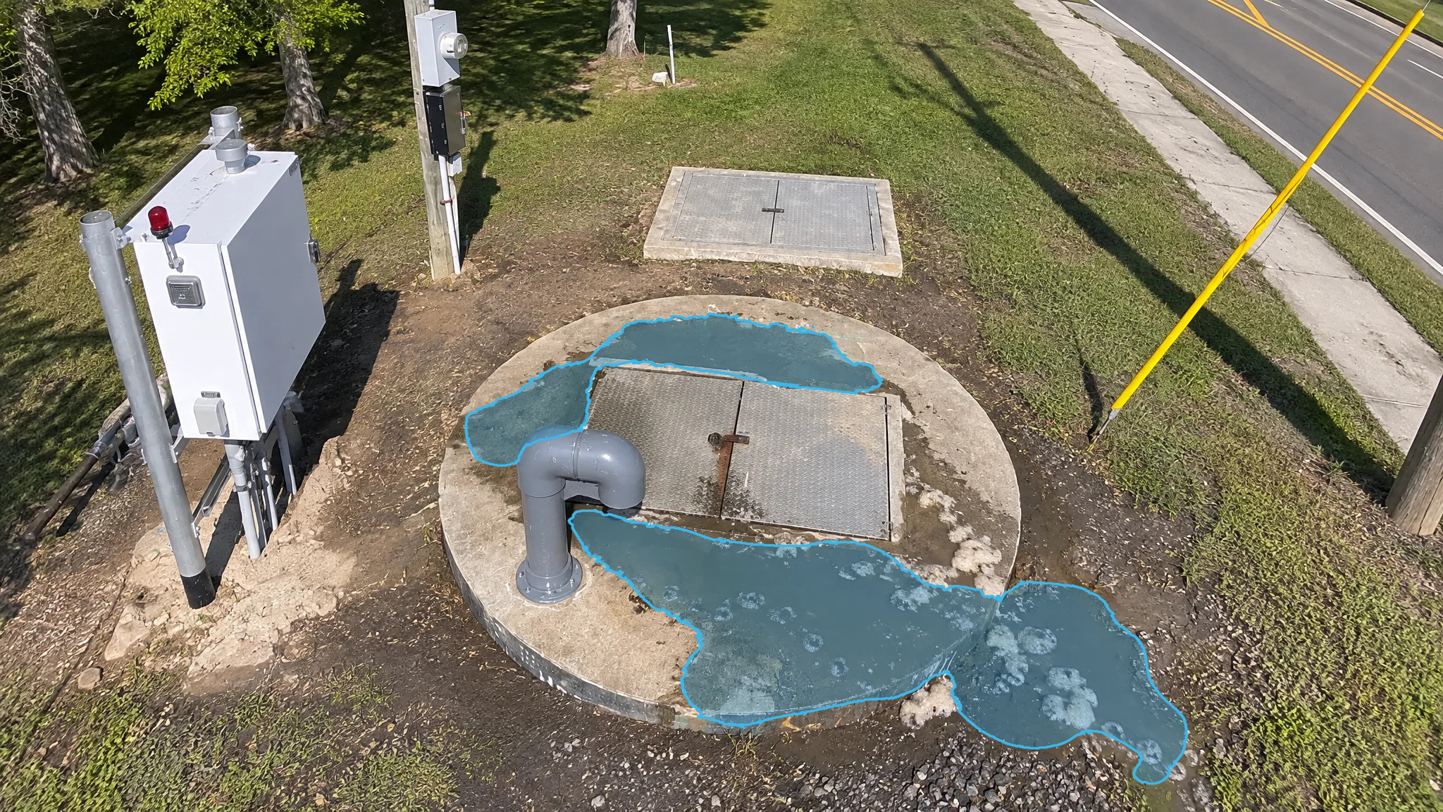 Lift station wet well hatch with blue detection overlays marking puddles spreading across the concrete pad.